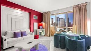 A modern living room with a white sofa, a coffee table, and a city view through large windows. - 777 Suite | Sphere + Strip View | Private Balcony (Las Vegas)