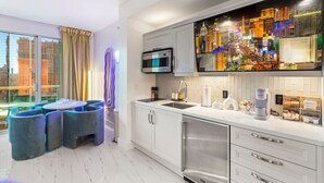 A modern kitchen with a large window, a dining area with blue chairs, and a cityscape view. - 777 Suite | Sphere + Strip View | Private Balcony (Las Vegas)