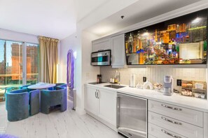 A modern kitchen with a large window, a dining area with blue chairs, and a cityscape view. - 777 Suite | Sphere + Strip View | Private Balcony (Las Vegas)