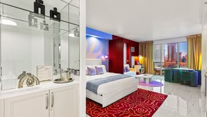 A modern hotel room with a large bed, a vanity with a mirror, a red patterned rug, and a city view through large windows. - 777 Suite | Sphere + Strip View | Private Balcony (Las Vegas)