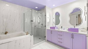 A modern bathroom with a glass-enclosed shower, a white bathtub, and purple vanity cabinets. - 777 Suite | Sphere + Strip View | Private Balcony (Las Vegas)