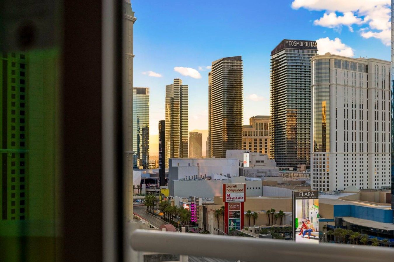 A cityscape with high-rise buildings, including The Cosmopolitan, and a visible street with palm trees and a Planet Hollywood sign.