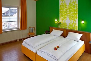 A double bed with white linens, a green accent wall, and a window with curtains. - Stadtcafé (Hammelburg)