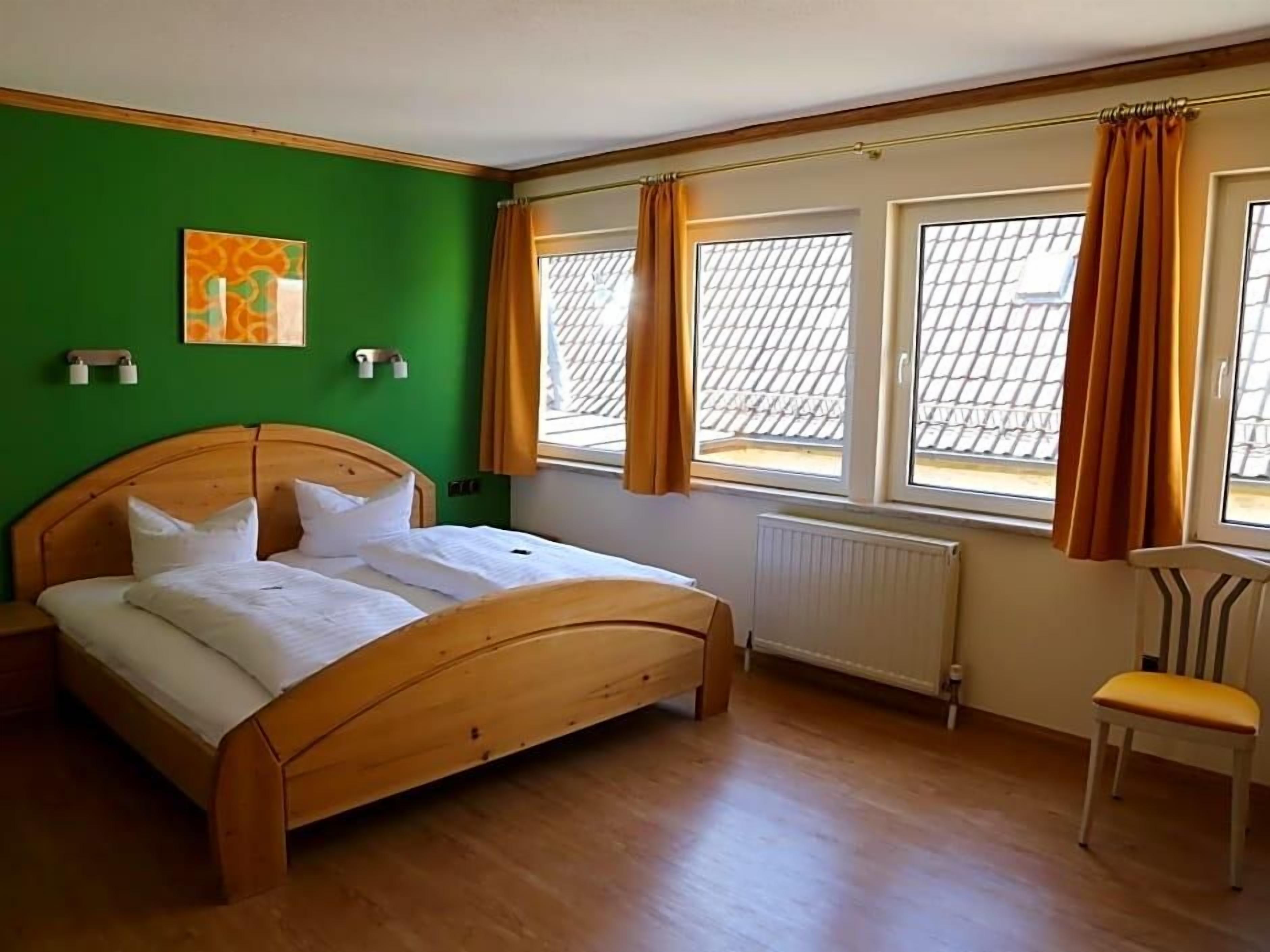 Ein Schlafzimmer mit einem hölzernen Bett, einem Heizkörper, einem Sessel und einem Fenster mit Vorhängen.