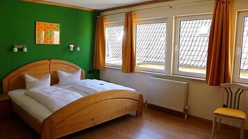Ein Schlafzimmer mit einem hölzernen Bett, einem Heizkörper, einem Sessel und einem Fenster mit Vorhängen.