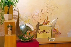 A reception desk with a 'RECEPTION' sign, a decorative metal sculpture, and a potted plant. - Stadtcafé (Hammelburg)