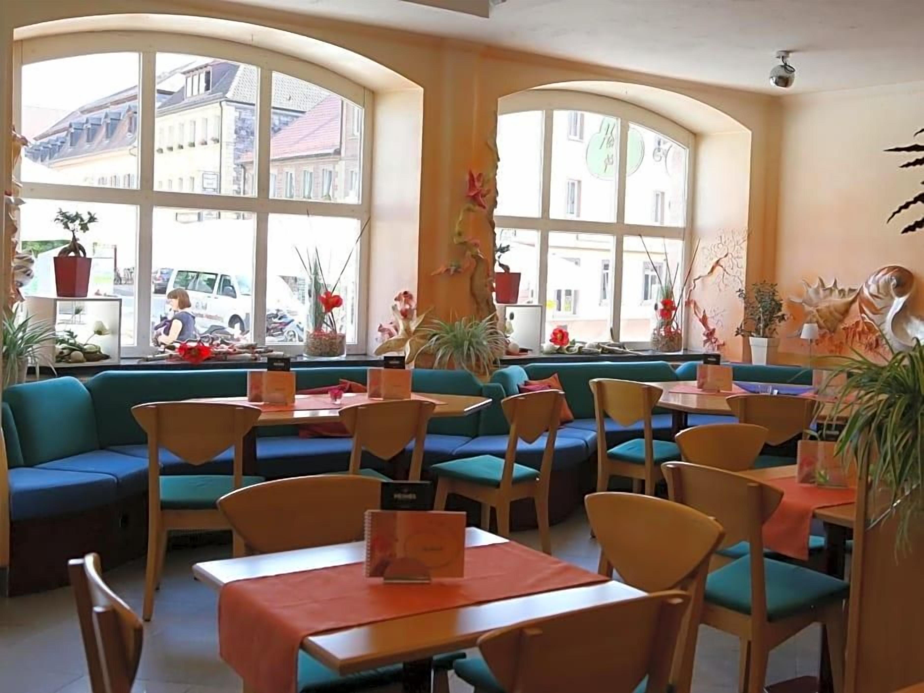 Ein Restaurant mit Sitzecken und Tischen, großen Fenstern und Topfpflanzen.