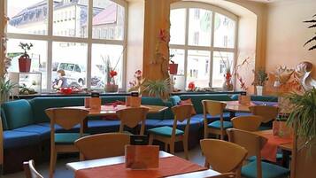 Ein Restaurant mit Sitzecken und Tischen, großen Fenstern und Topfpflanzen.