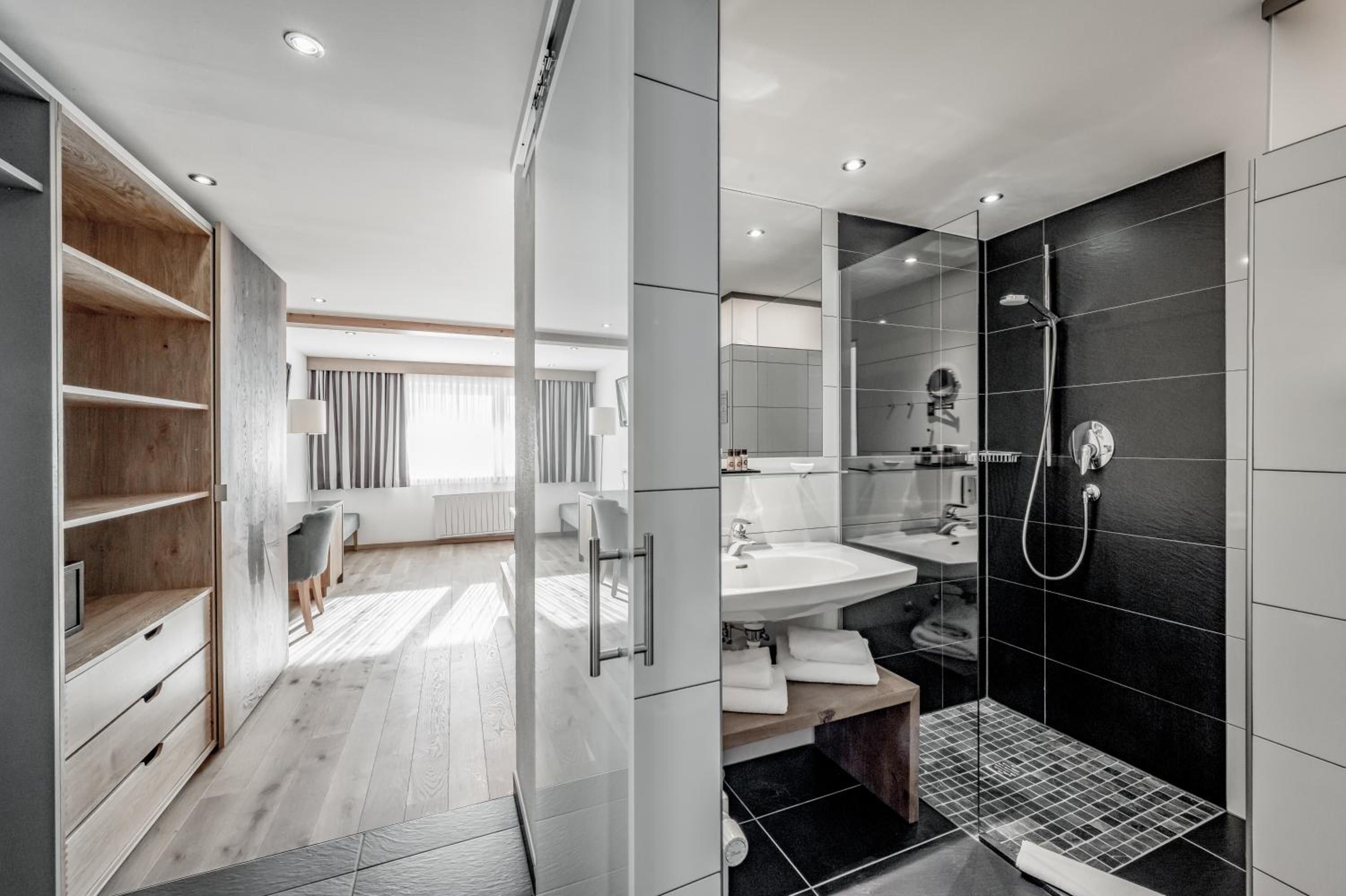 A modern bathroom with a walk-in shower, a vanity with a sink, and a wooden vanity with open shelving.