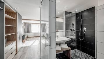 A modern bathroom with a walk-in shower, a vanity with a sink, and a wooden vanity with open shelving.