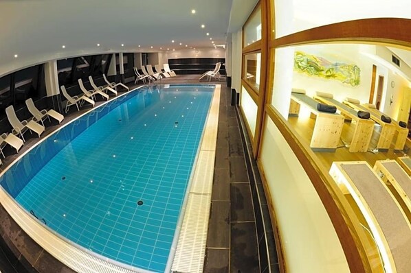 Ein großer, überdachter Pool mit gefliestem Boden, umgeben von Liegestühlen und einer Rezeption mit Holztresen.