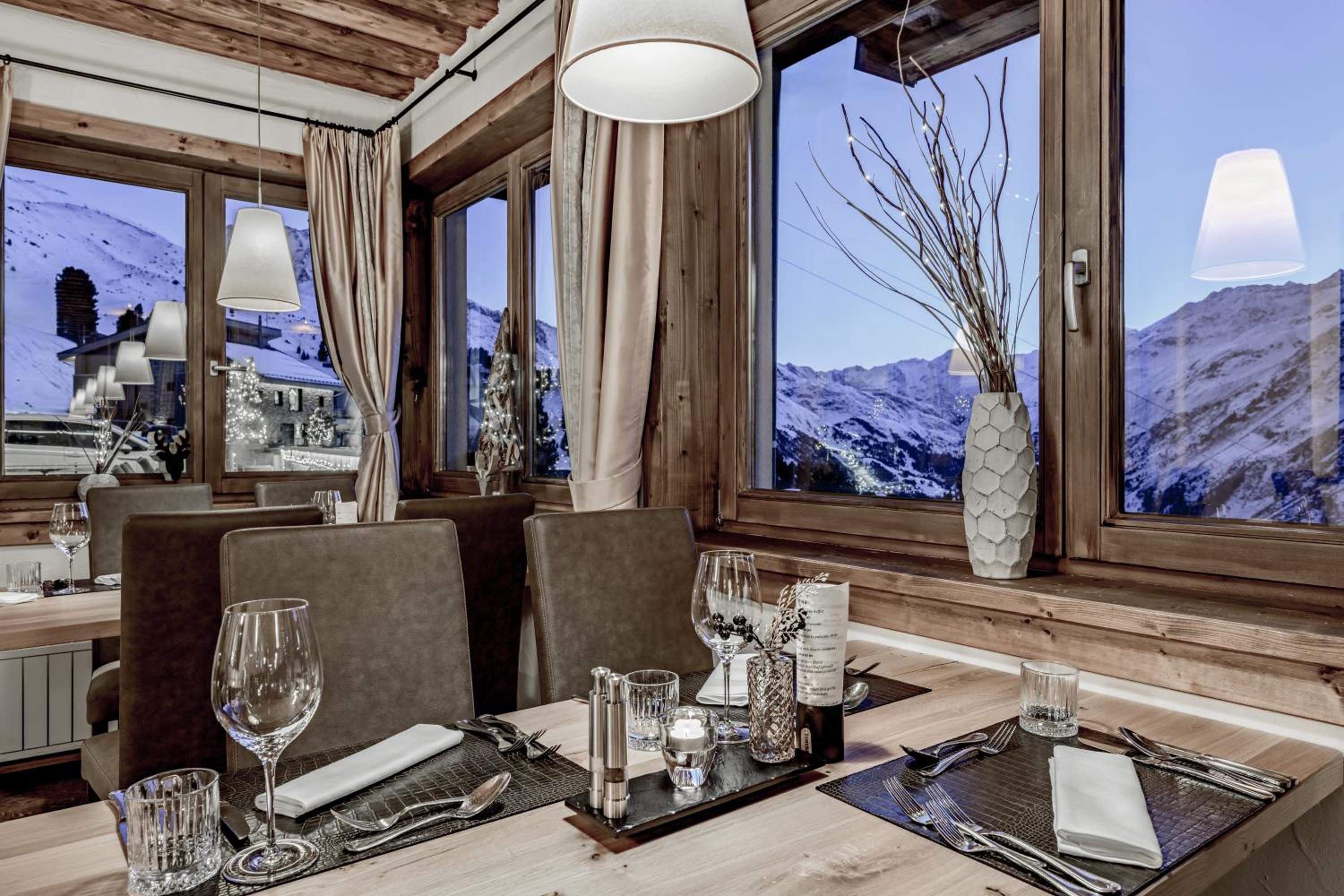 A restaurant with a wooden interior, large windows with mountain views, and a table set for dining.