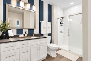 Un baño moderno con un espejo grande, muebles blancos, cabina de ducha y una pequeña planta en el tocador.