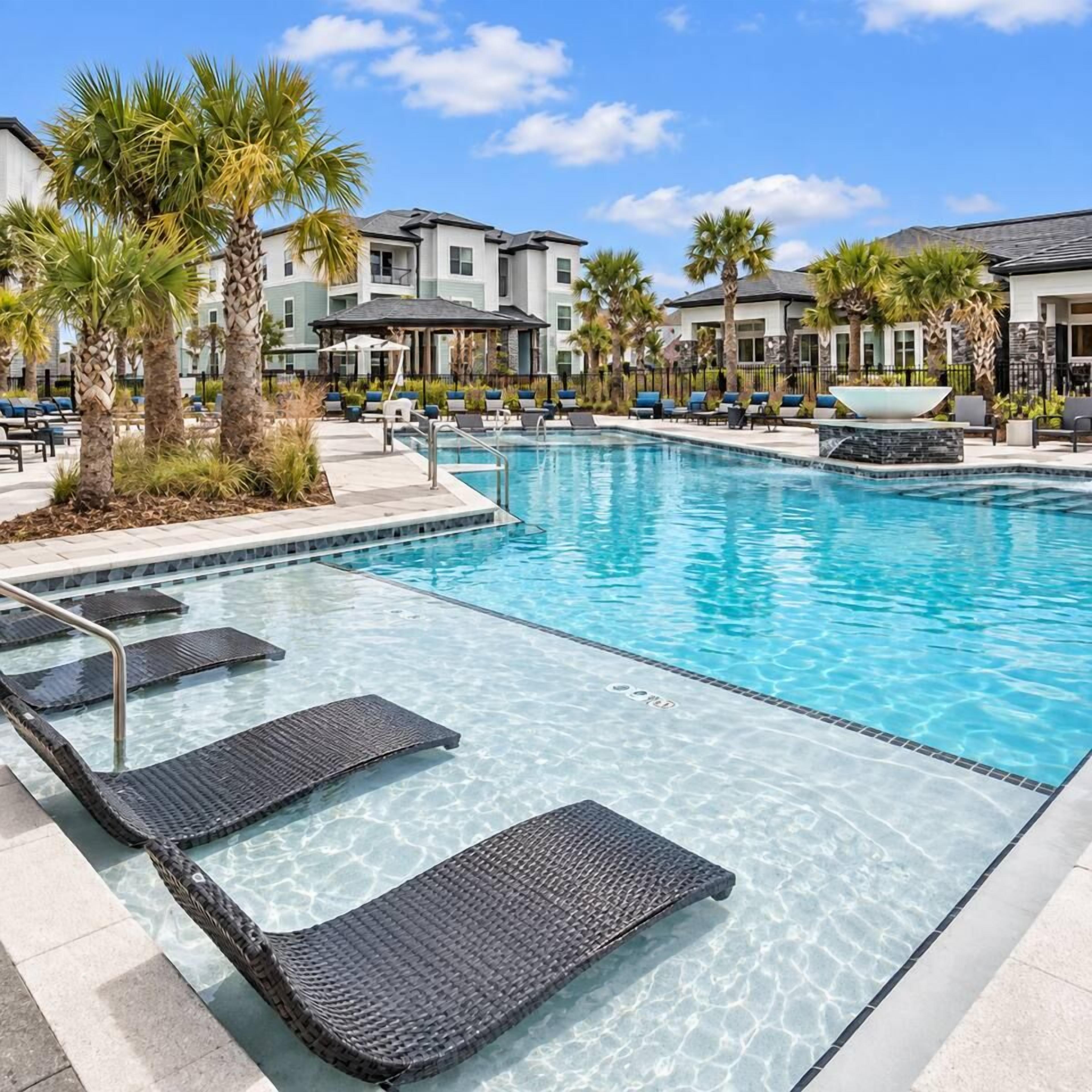 A swimming pool with clear water, surrounded by lounge chairs and palm trees.