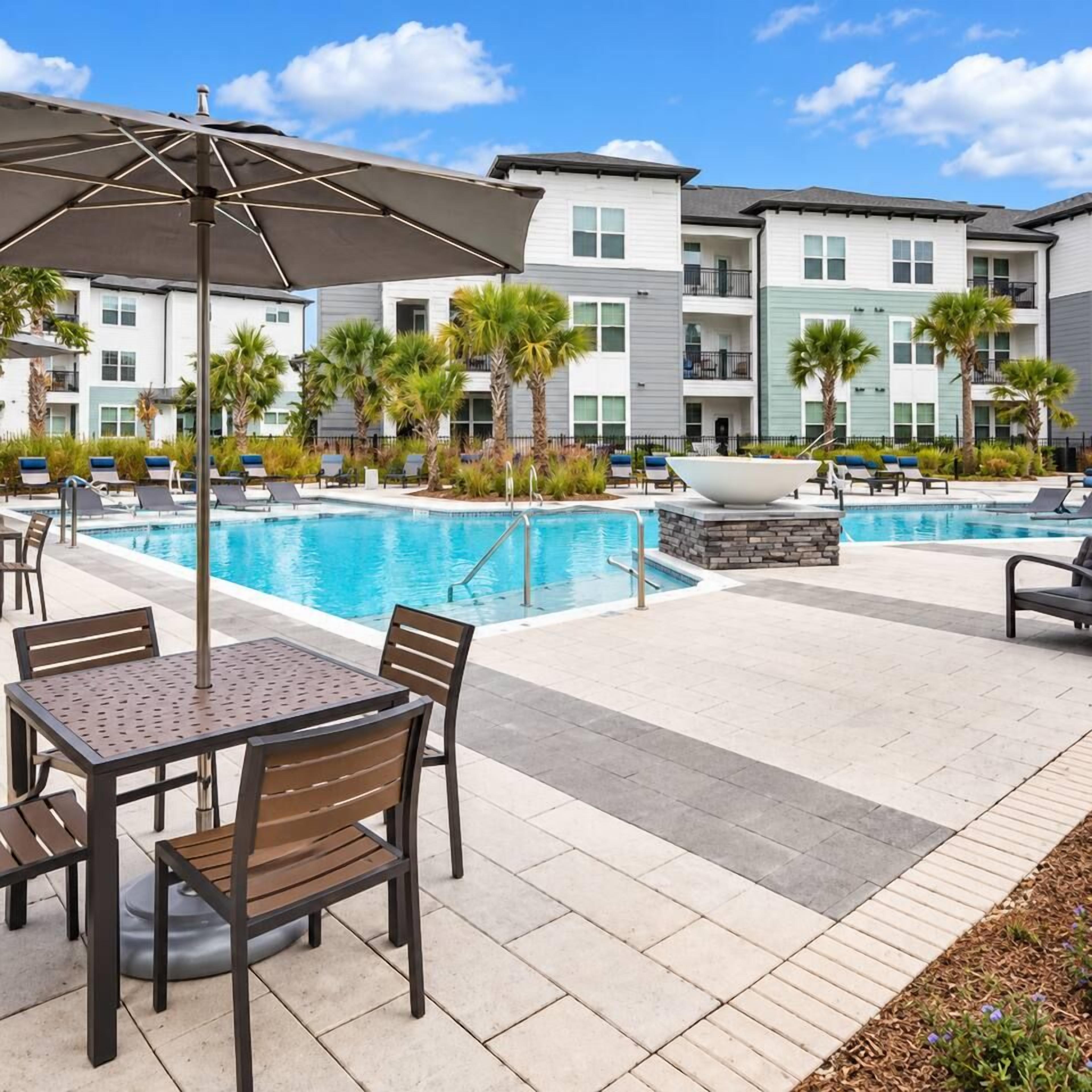 Un espace aménagé au bord de la piscine, avec des chaises longues, une table et un grand parasol.