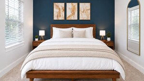 Un dormitorio con cama de madera, ropa de cama blanca, dos lámparas de noche y una obra de arte abstracta en la pared.