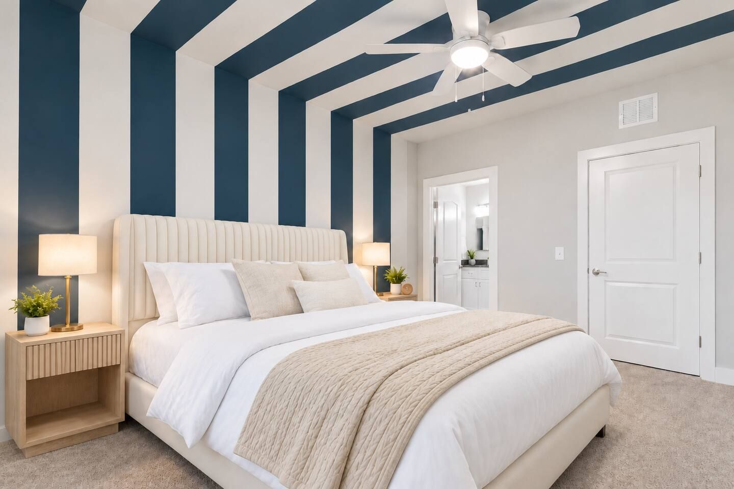 A bedroom with a large bed, bedside tables, a ceiling fan, and a door leading to another room.