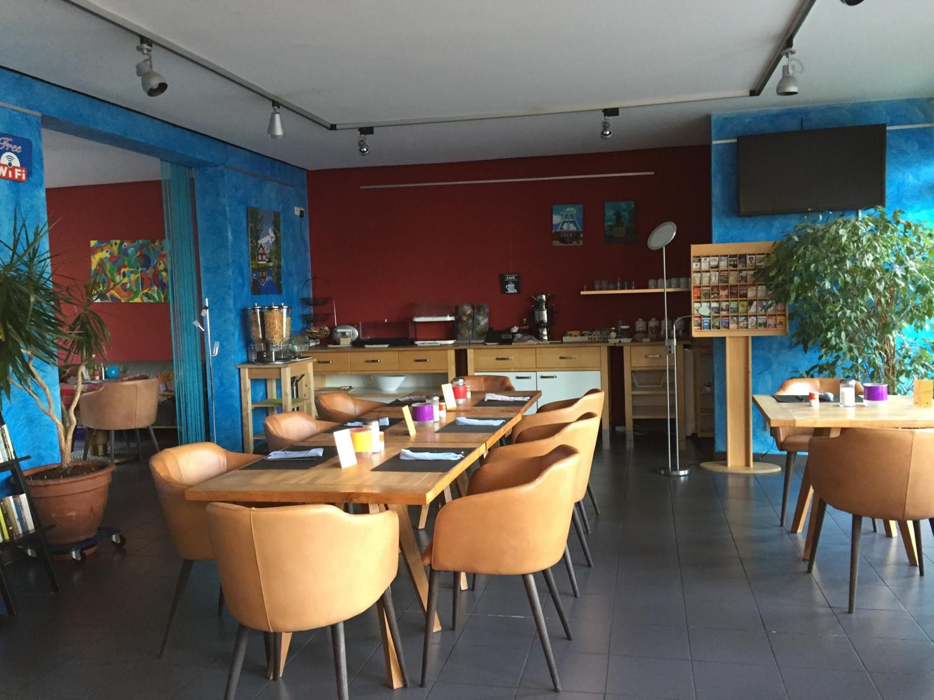 Ein Restaurant mit einer langen Theke, mehreren Tischen und Stühlen. An den Wänden befinden sich Blumentöpfe und Kunstwerke.