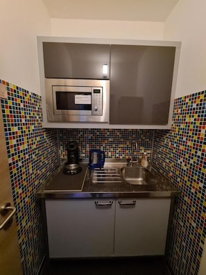 Cocina compacta con microondas, cafetera y lavamanos.