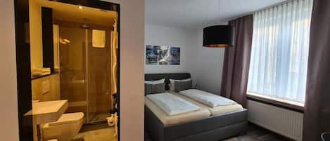 A modern hotel room with a shower, toilet, bed, and a large window with curtains.