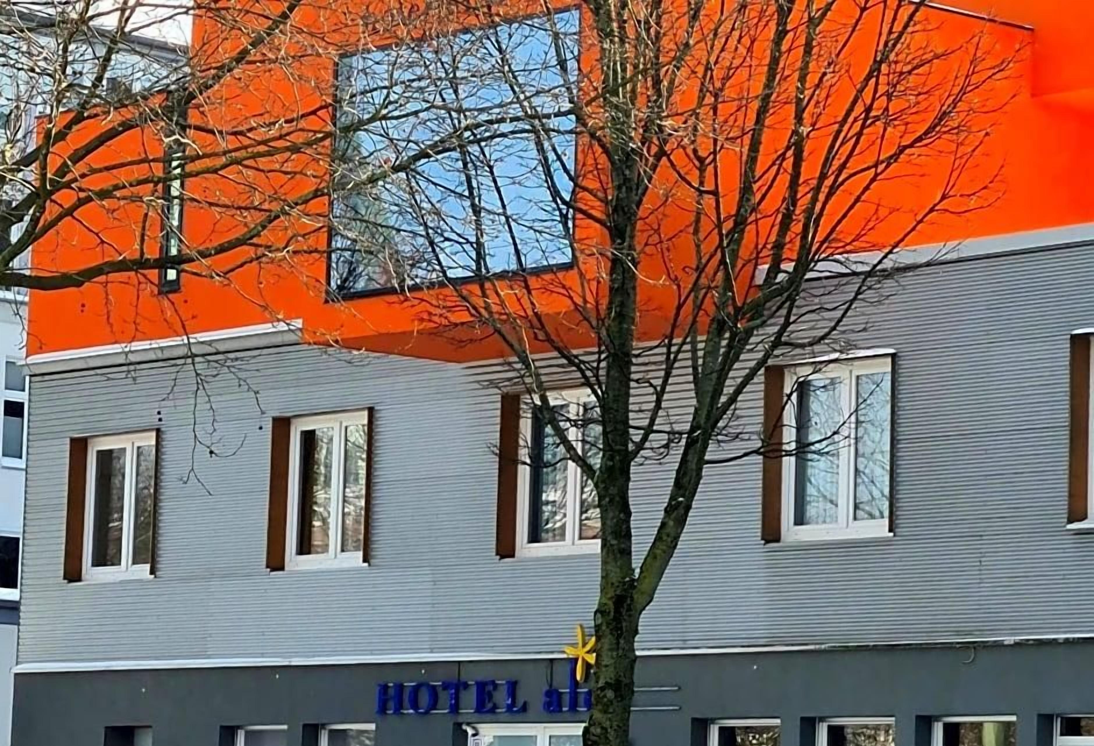 A hotel with a grey facade and an orange section, featuring a sign with the hotel's name.