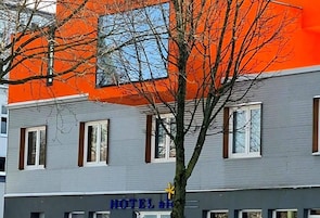 A hotel with a grey facade and an orange section, featuring a sign with the hotel's name.