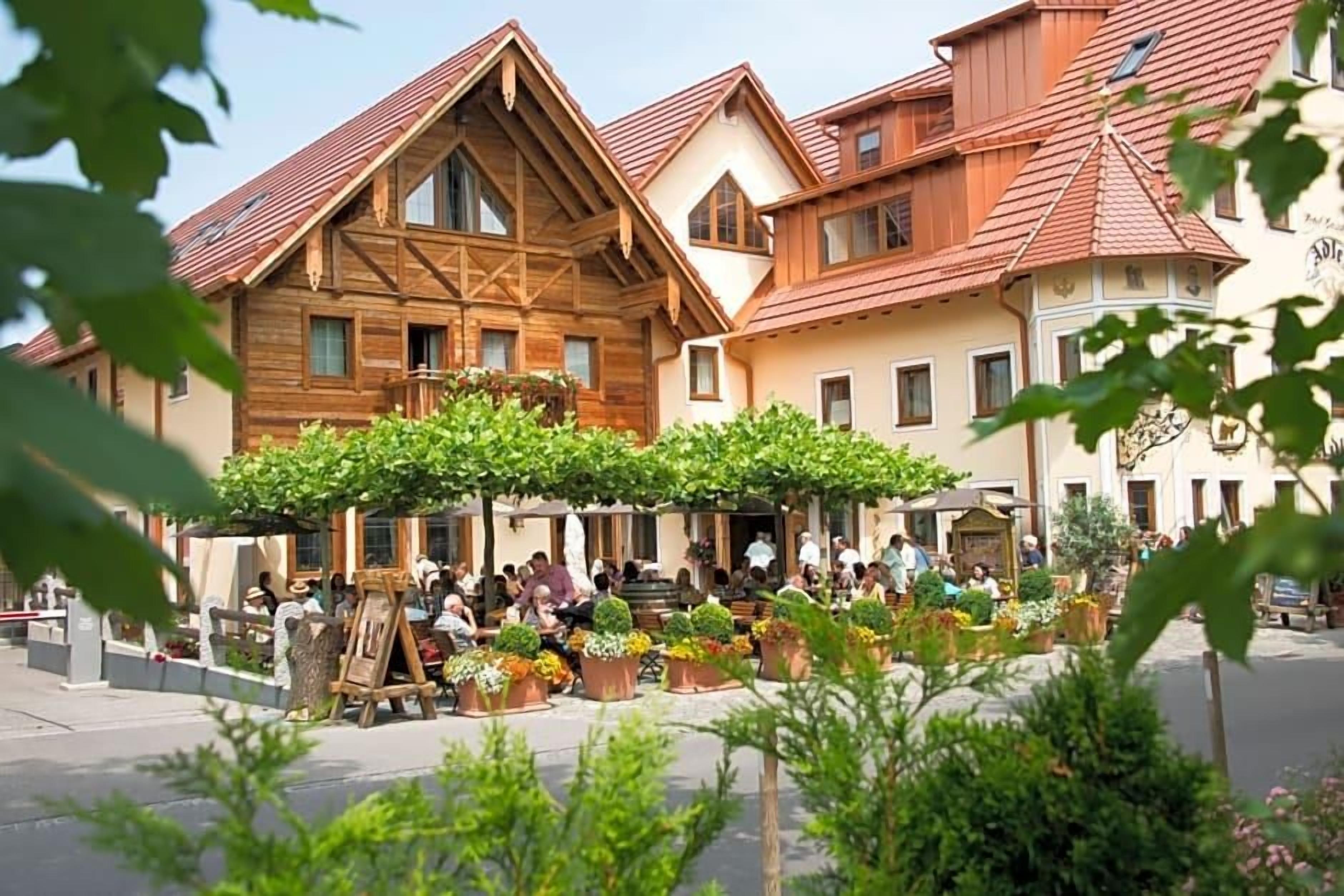 Ein traditionelles europäisches Gebäude mit einer Holzfassade, einem Balkon und einem Innenhof mit Blumentöpfen und Sitzgelegenheiten.