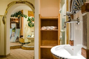 Un baño con estante de madera que sostiene toallas, un lavabo y un espejo.