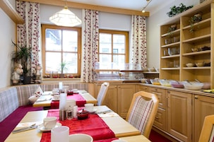 Un comedor con una mesa dispuesta para dos, una ventana con cortinas florales y un mueble de madera con estantes.