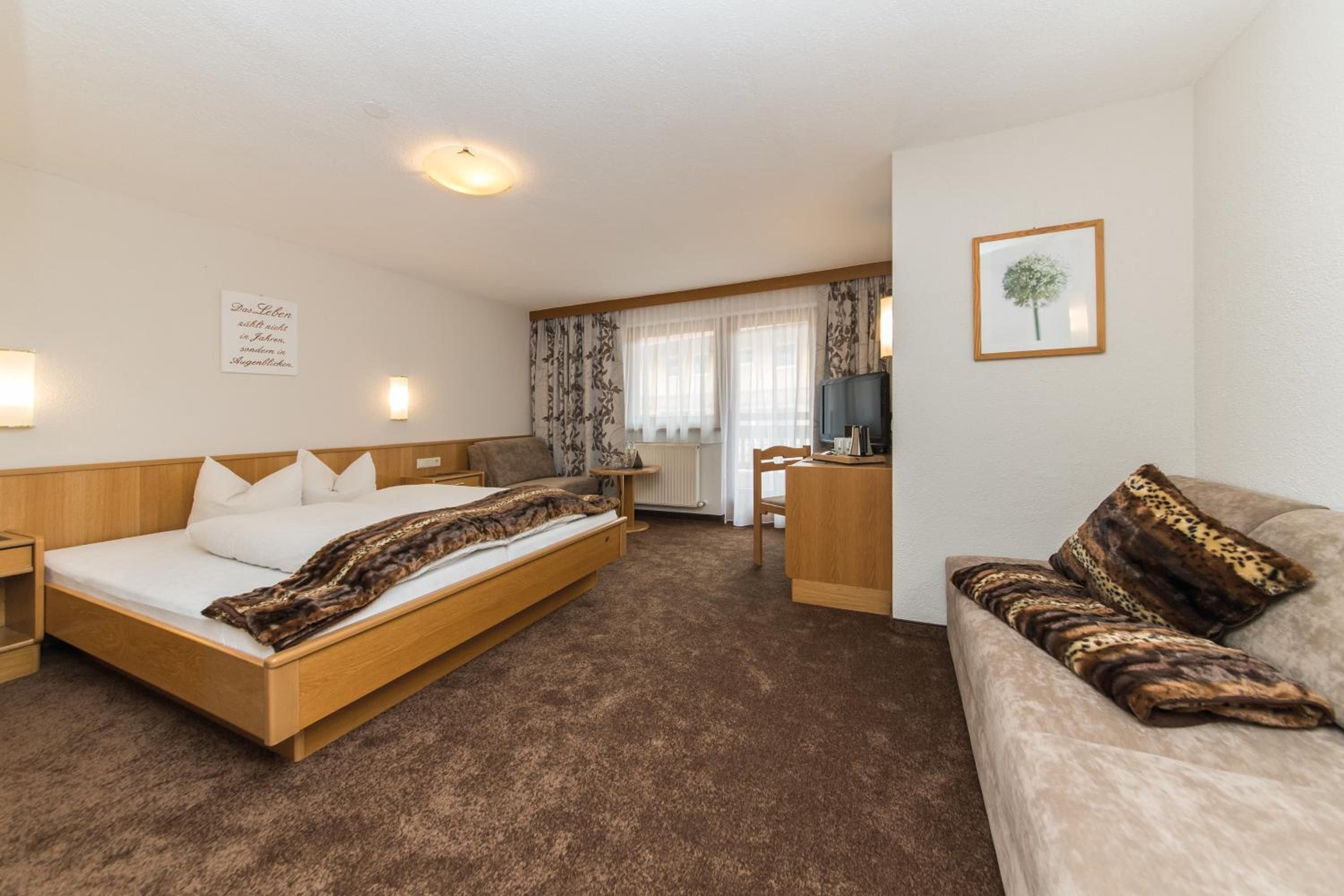 A hotel room with a bed, a sofa, a desk, and a television.