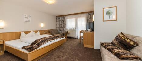 A hotel room with a bed, a sofa, a desk, and a television.
