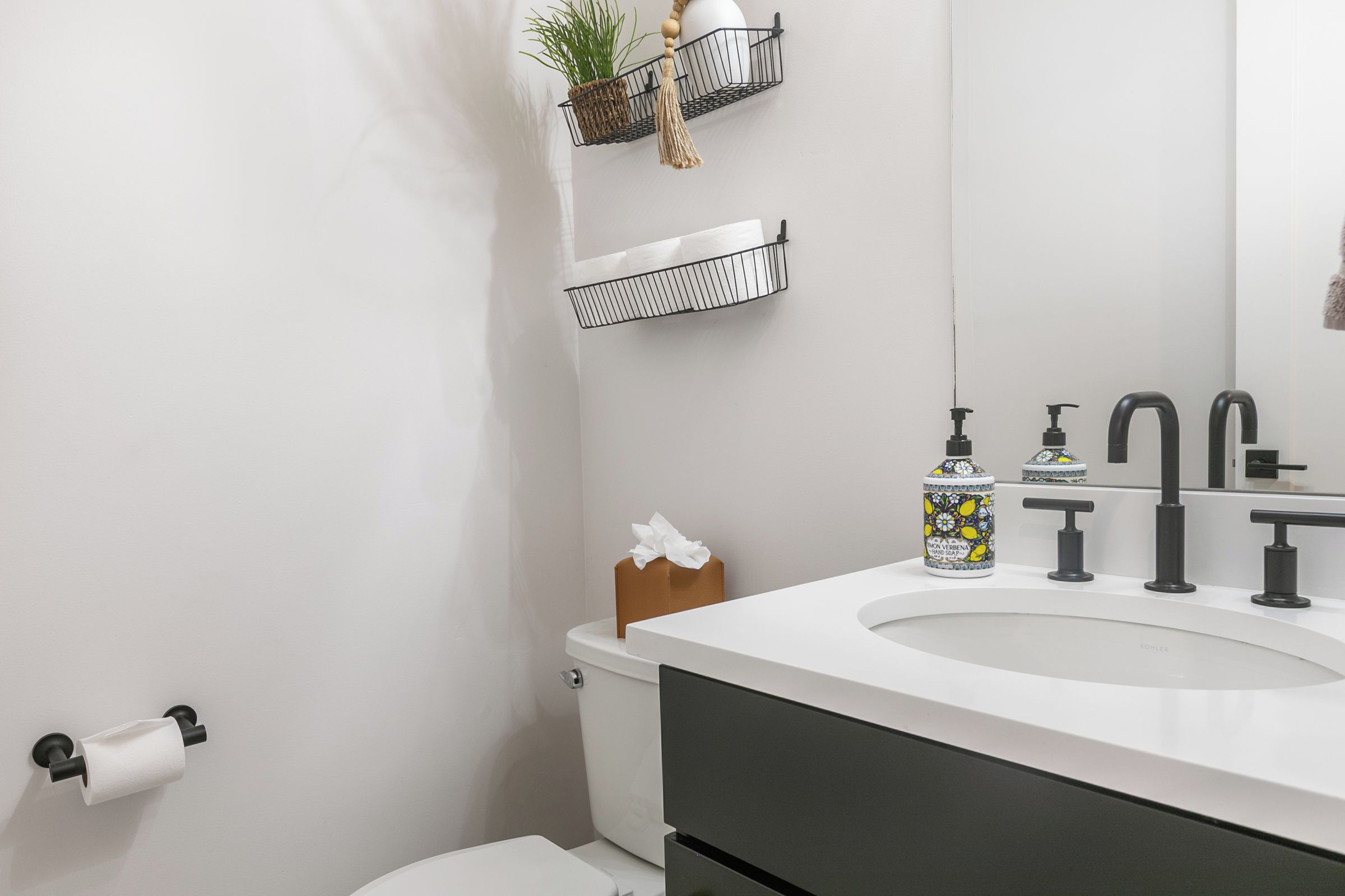 A modern bathroom with a white sink, black faucets, and a toilet paper holder.