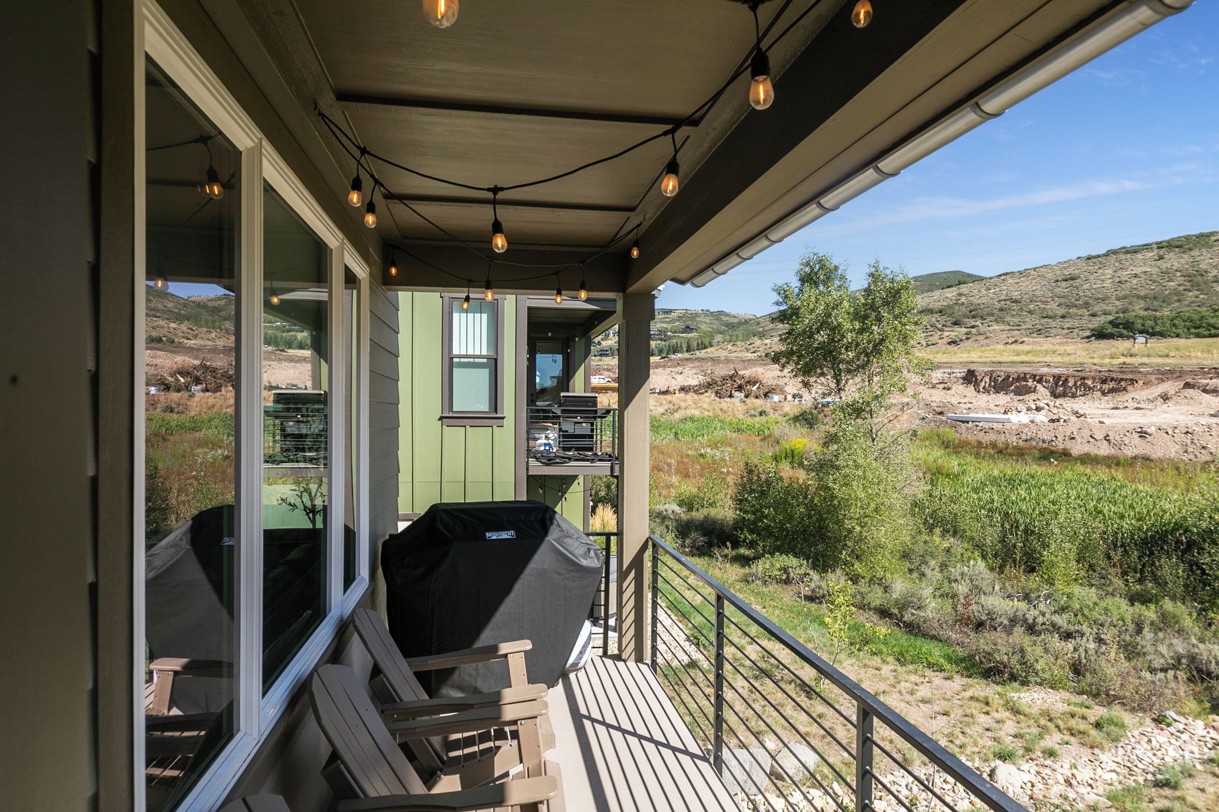 A covered outdoor area with a barbecue grill, seating, and a view of a hilly landscape.