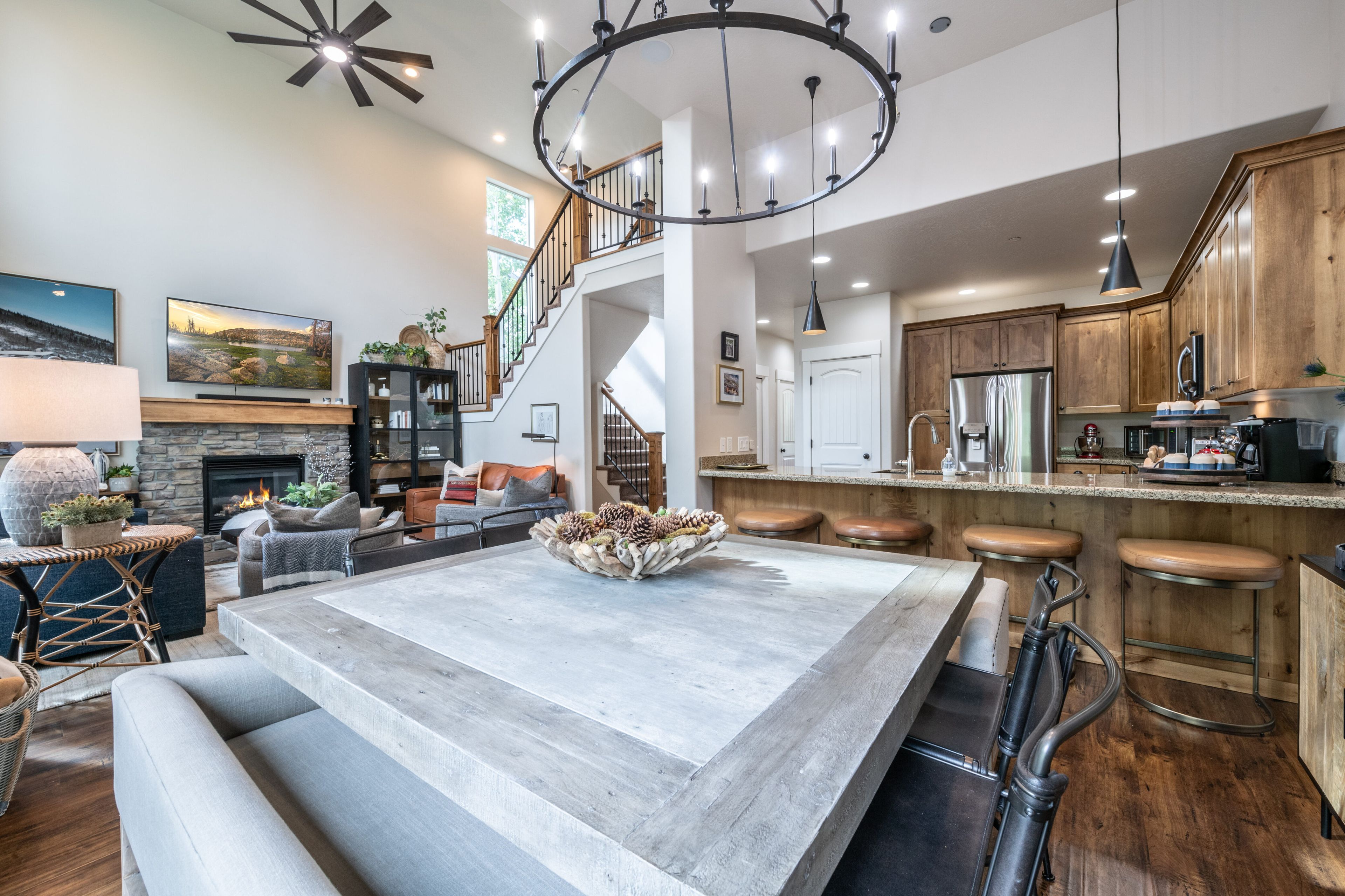 A spacious living area with a large dining table, a fireplace, and a staircase leading to an upper level.