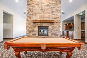 Une table de billard dans une pièce dotée d’une cheminée en pierre et de meubles en bois.