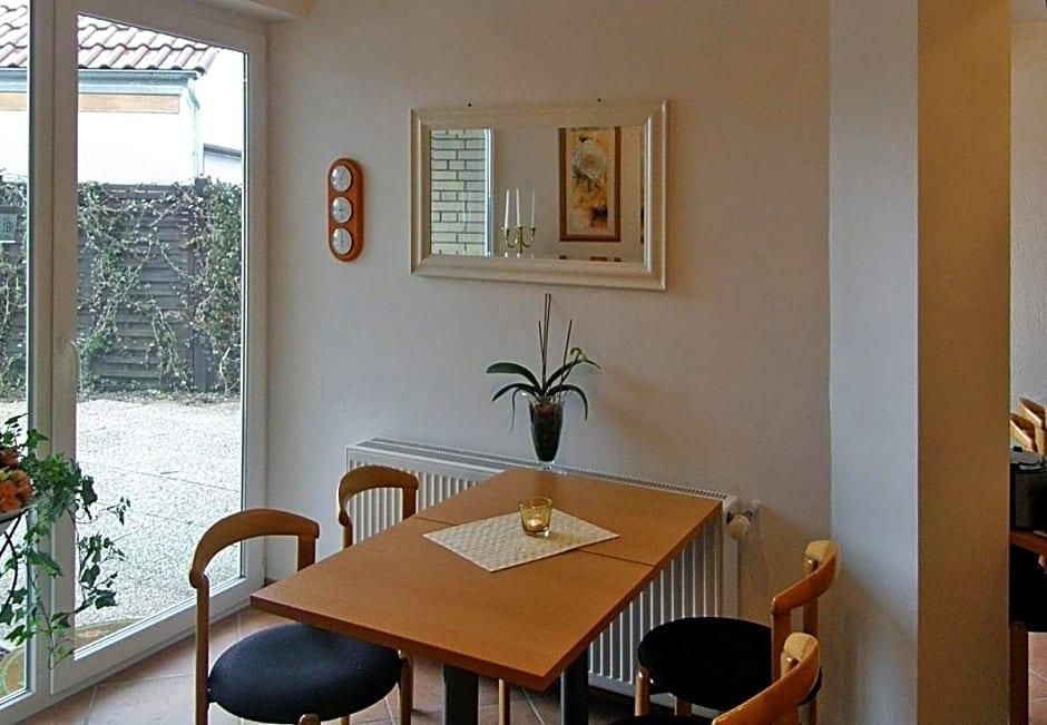 Een eetgedeelte met een tafel, stoelen, een potplant, een ingelijst kunstwerk en een wandklok.