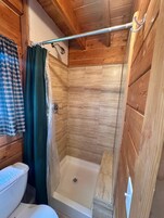 Zona de ducha con techo de madera, cortina de ducha y bañera blanca.