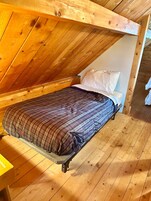Un dormitorio estilo loft con techo inclinado, cama con cubrecama a cuadros y piso de madera.