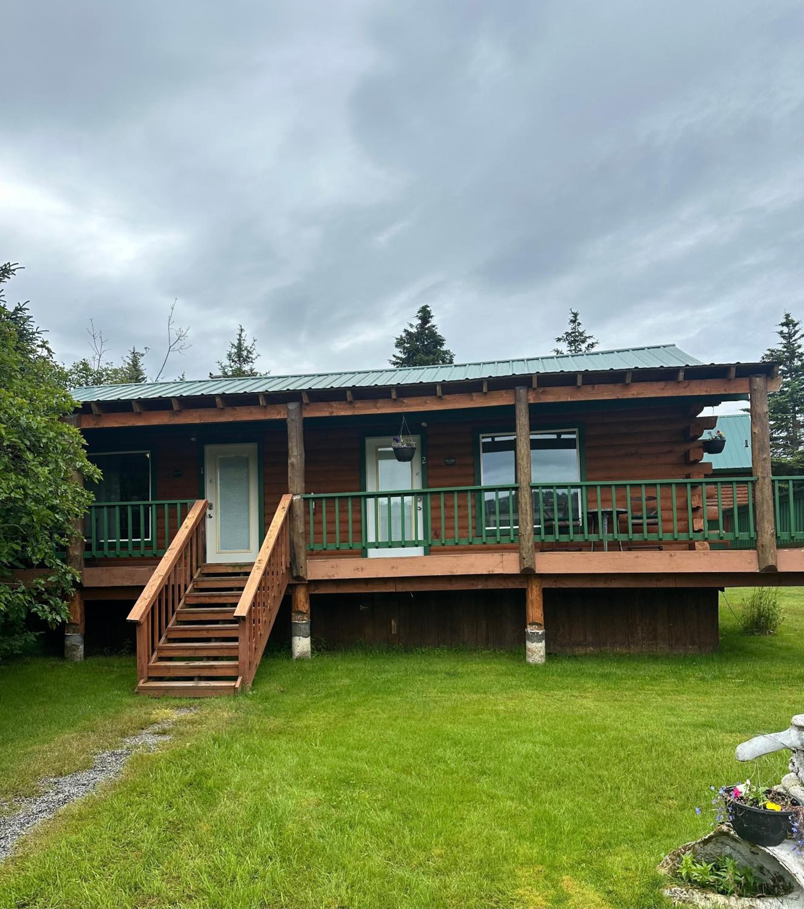 A two-story log cabin with a wooden deck and a staircase leading to the upper level.