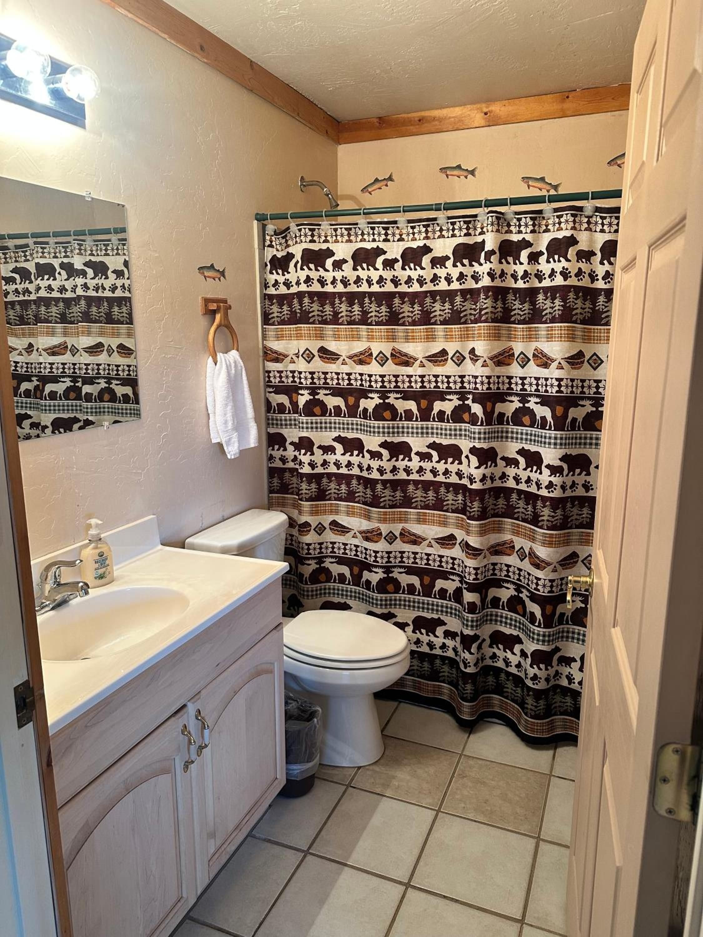 A bathroom with a toilet, sink, and shower curtain featuring animal patterns.
