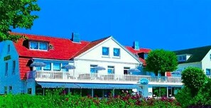 A two-story building with a white facade, red roof, and a balcony with umbrellas. - Seelust (Hohwacht)