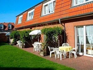 Un edificio de ladrillo con techo rojo, ventanas con marcos blancos y un patio empaved con mobiliario exterior.
