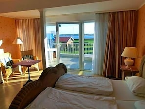 A hotel room with a bed, a table, a chair, and a view of the outdoors. - Seelust (Hohwacht)
