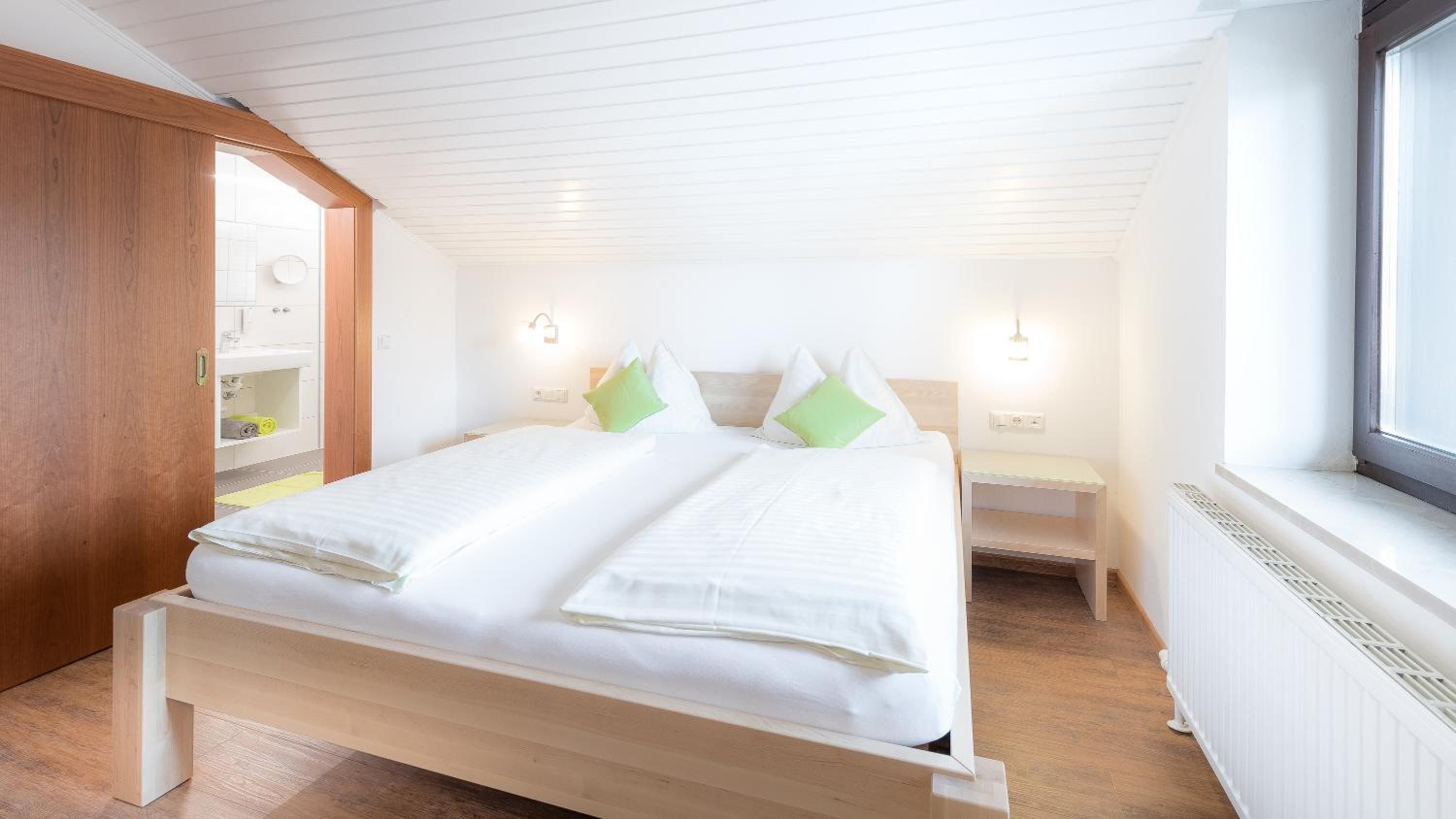 Une chambre à coucher avec un lit en bois, deux tables de chevet, une fenêtre et une armoire intégrée.