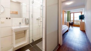 Ein Hotelzimmer mit Dusche, Waschbecken, Bett, Schreibtisch und Fernseher.