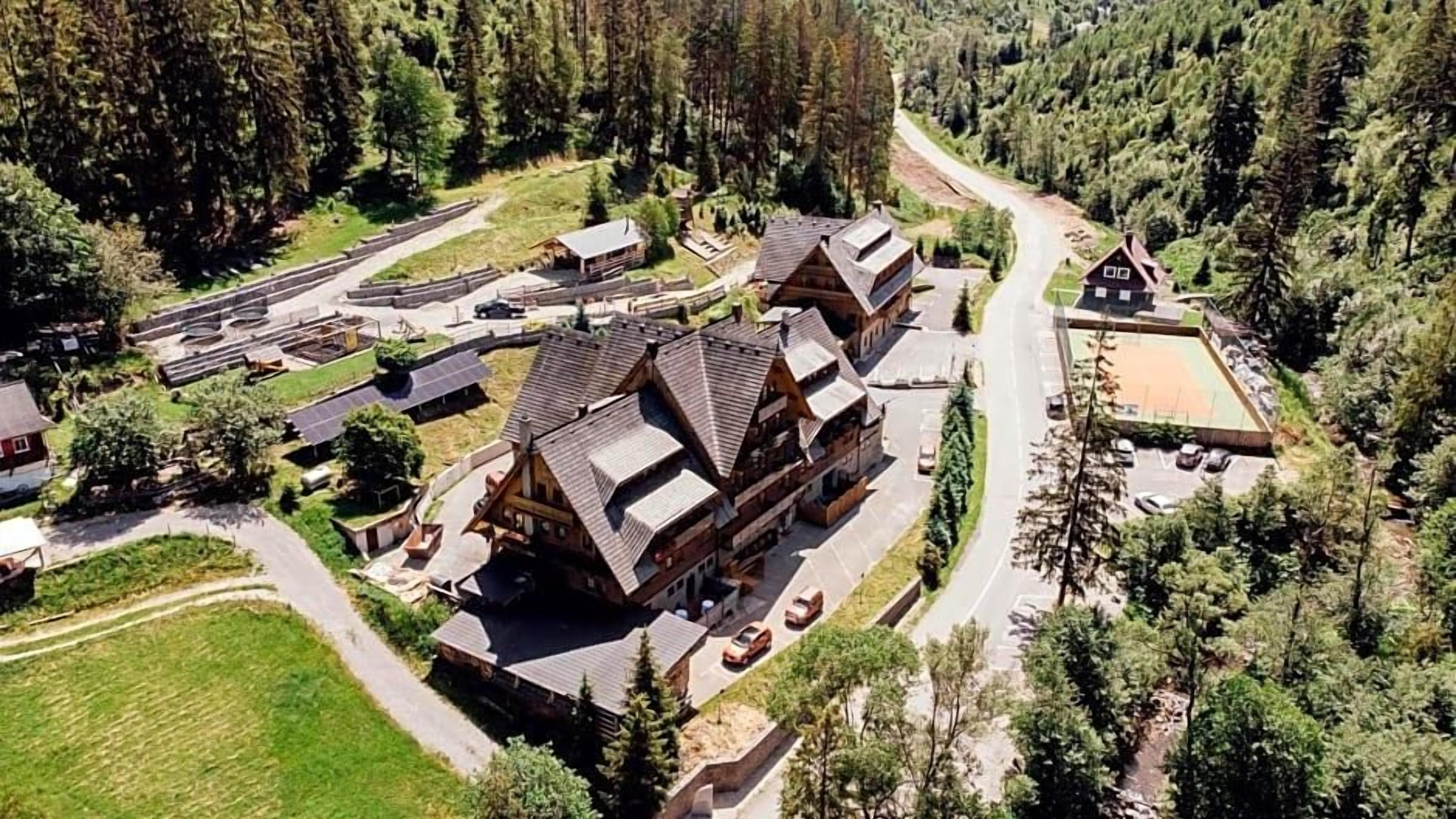 Un chalet comprenant plusieurs bâtiments, un espace de stationnement et une forêt environnante.