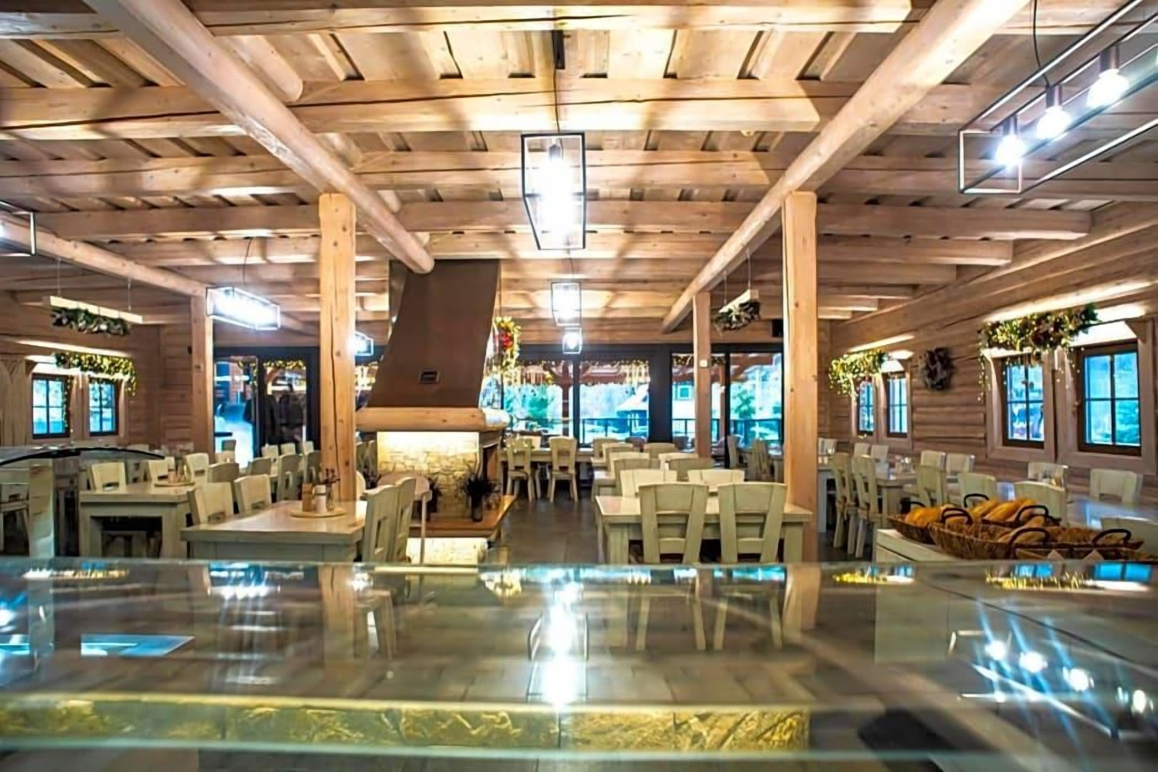 A spacious indoor area with wooden beams on the ceiling, tables, chairs, and a central decorative element.