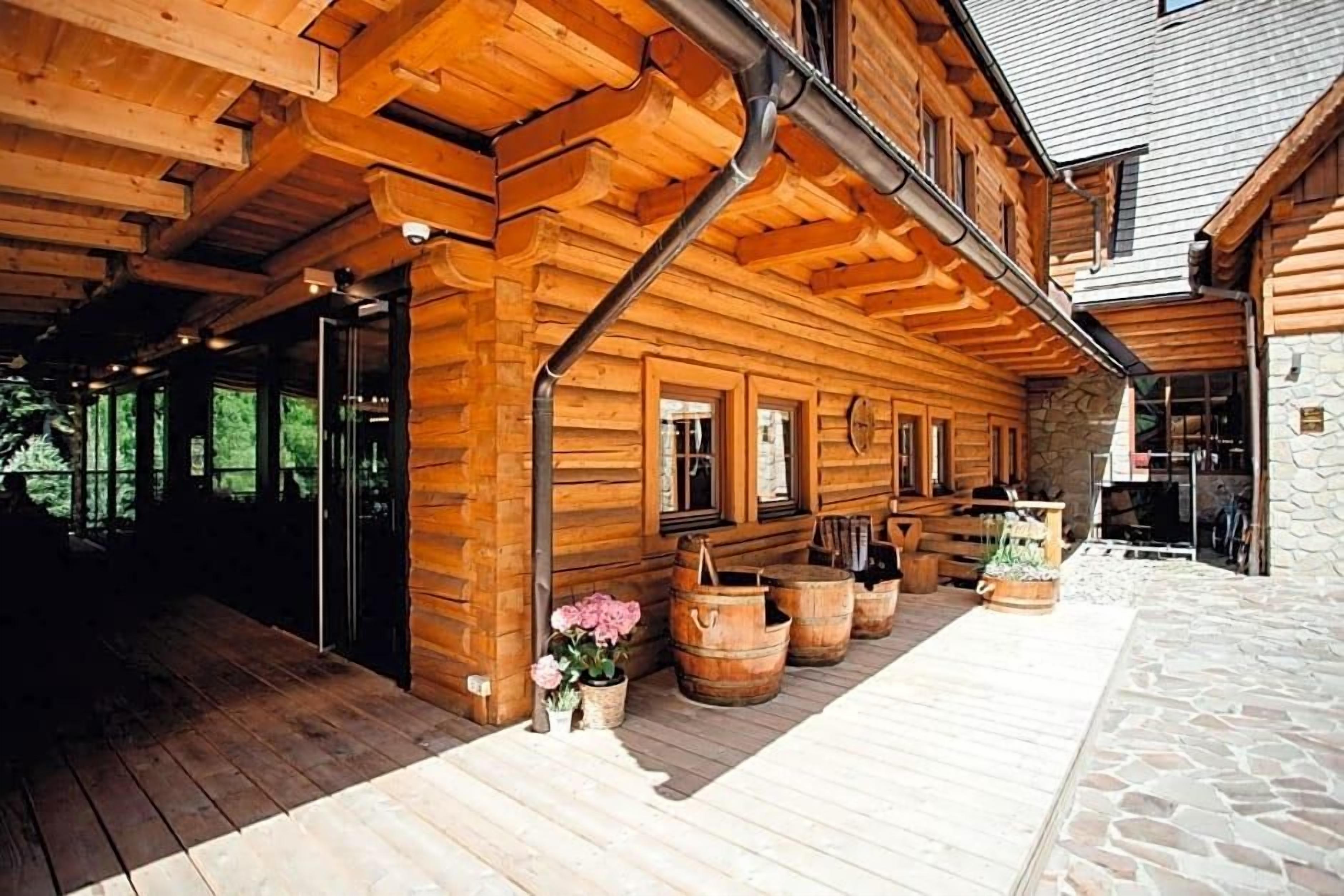 A wooden cabin with a porch, stone walls, and wooden barrels.