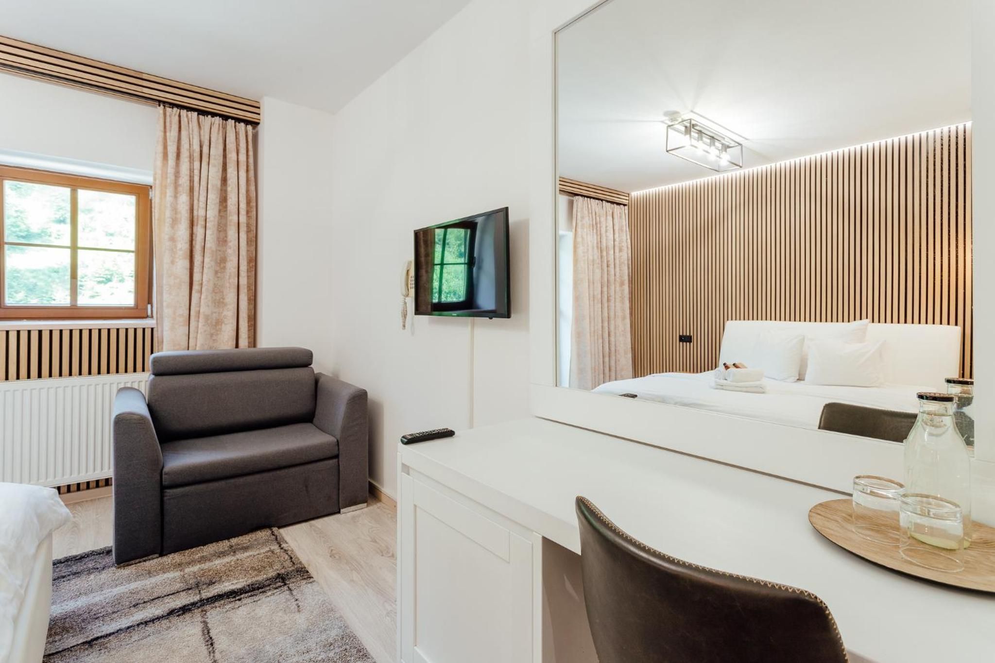 Una habitación de hotel moderna con sofá, cama, televisor y un espejo grande.