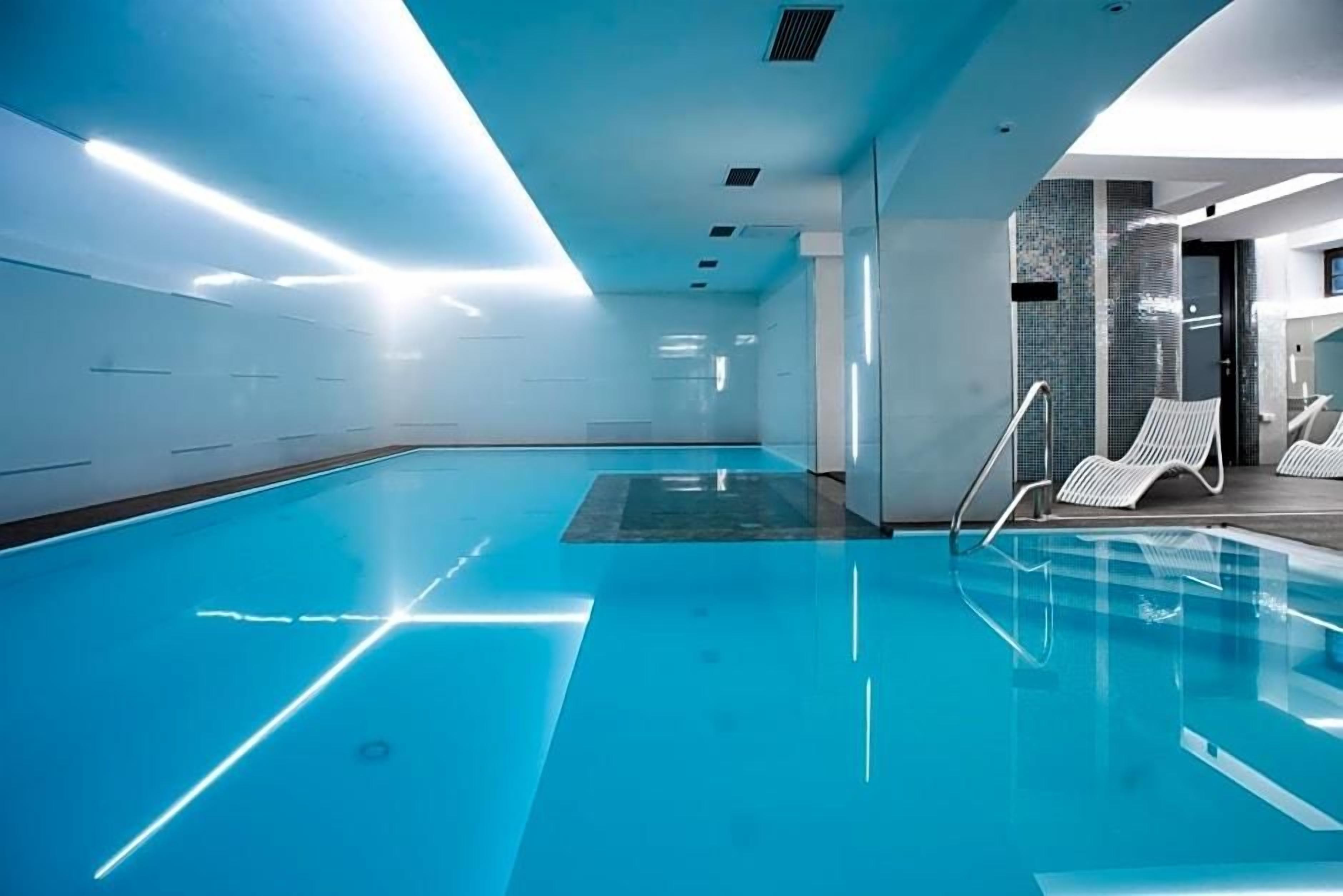 Une piscine intérieure moderne avec de l’eau cristalline, un plafond laissant entrer la lumière du soleil et des chaises longues disposées au bord du bassin.